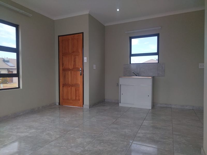 A clean, empty kitchen area featuring tiled flooring, a single basin sink with a tiled splashback, and neutral wall tones.