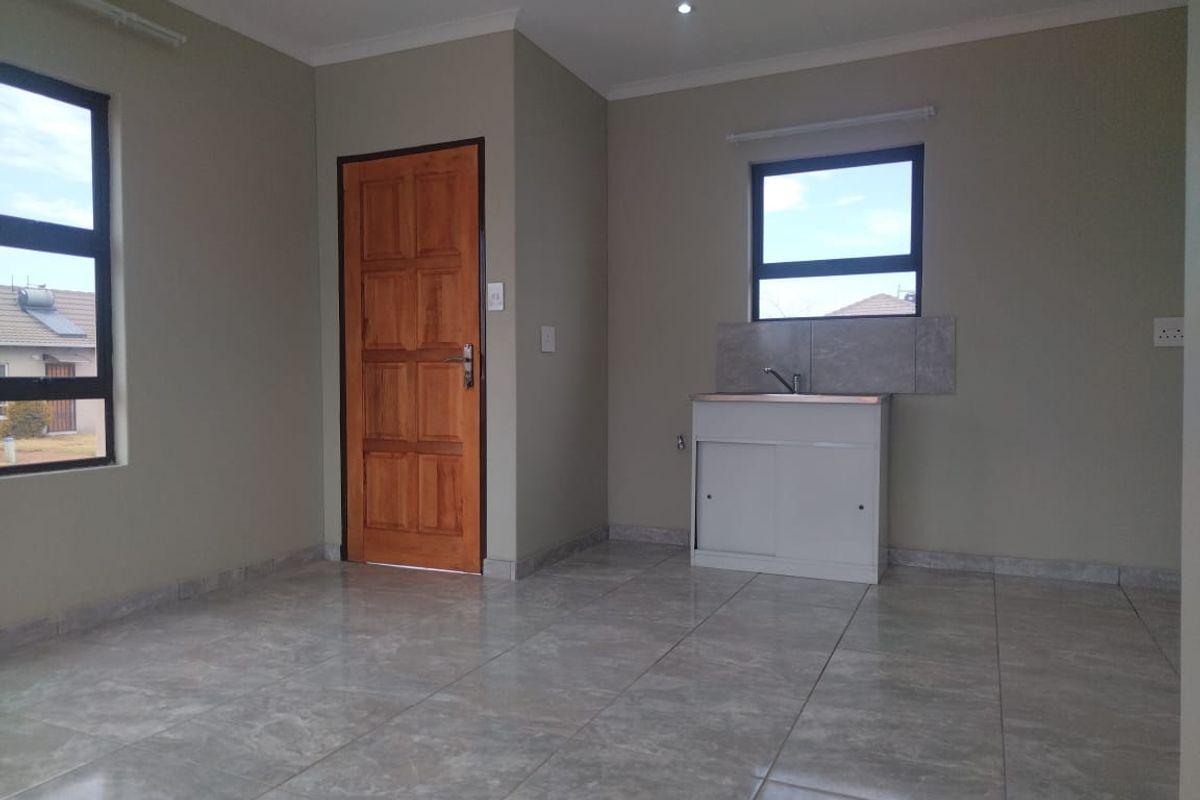A clean, empty kitchen area featuring tiled flooring, a single basin sink with a tiled splashback, and neutral wall tones.