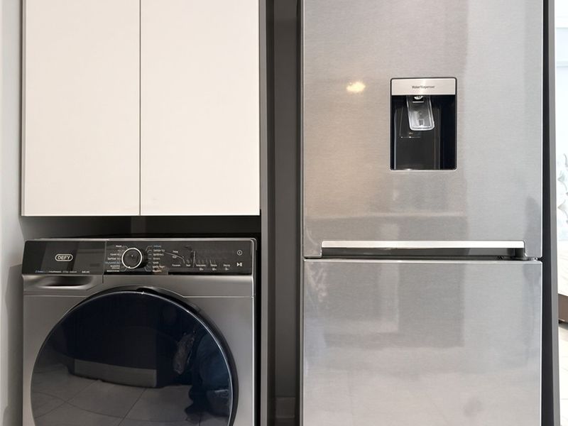A compact laundry area featuring modern built-in cabinetry and tiled flooring, designed to accommodate a washing machine and refrigerator.