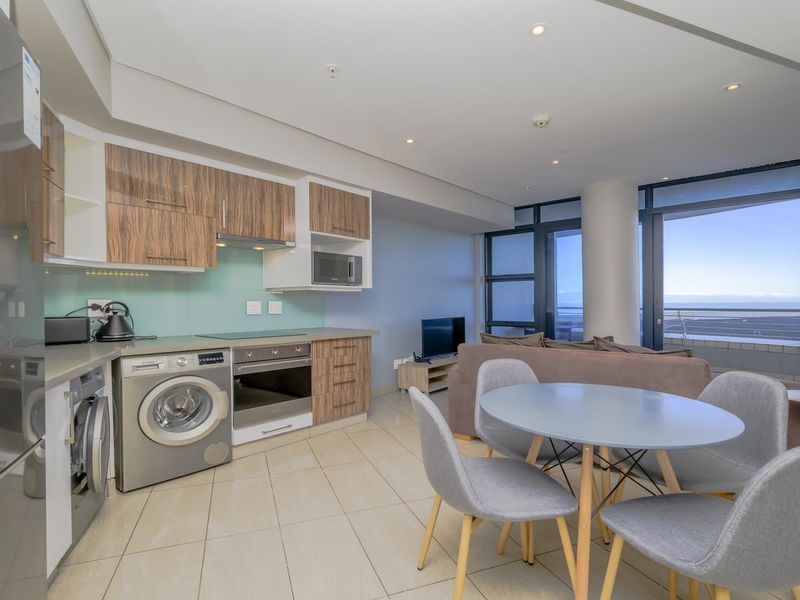 Modern open-plan apartment featuring a sleek kitchen with integrated appliances, tiled flooring, and expansive floor-to-ceiling windows offering natural light and scenic views.