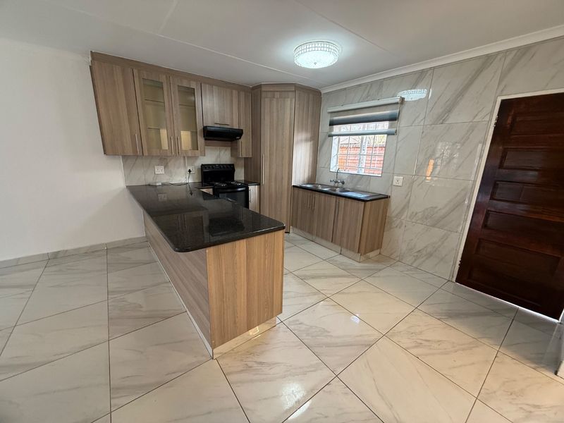 Modern kitchen featuring granite countertops, laminate cabinetry, marble-effect wall tiles, and tiled flooring in an open-plan layout.