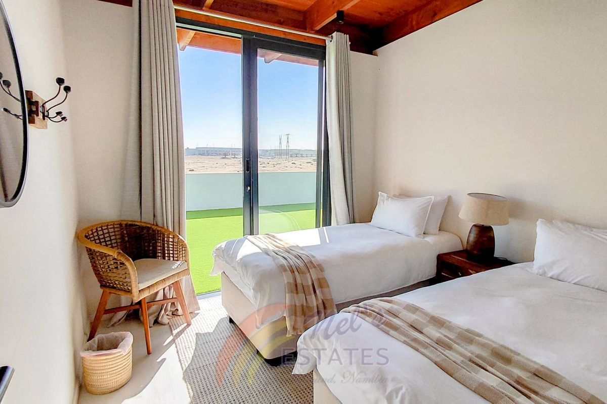 A bright bedroom featuring exposed timber ceiling beams and large sliding glass doors that open onto a private balcony with scenic views.