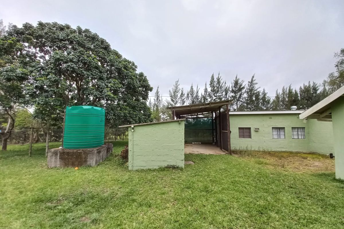Exterior view of a small holding outbuilding featuring a water storage tank, covered workspace, and basic masonry construction set in a rural garden.