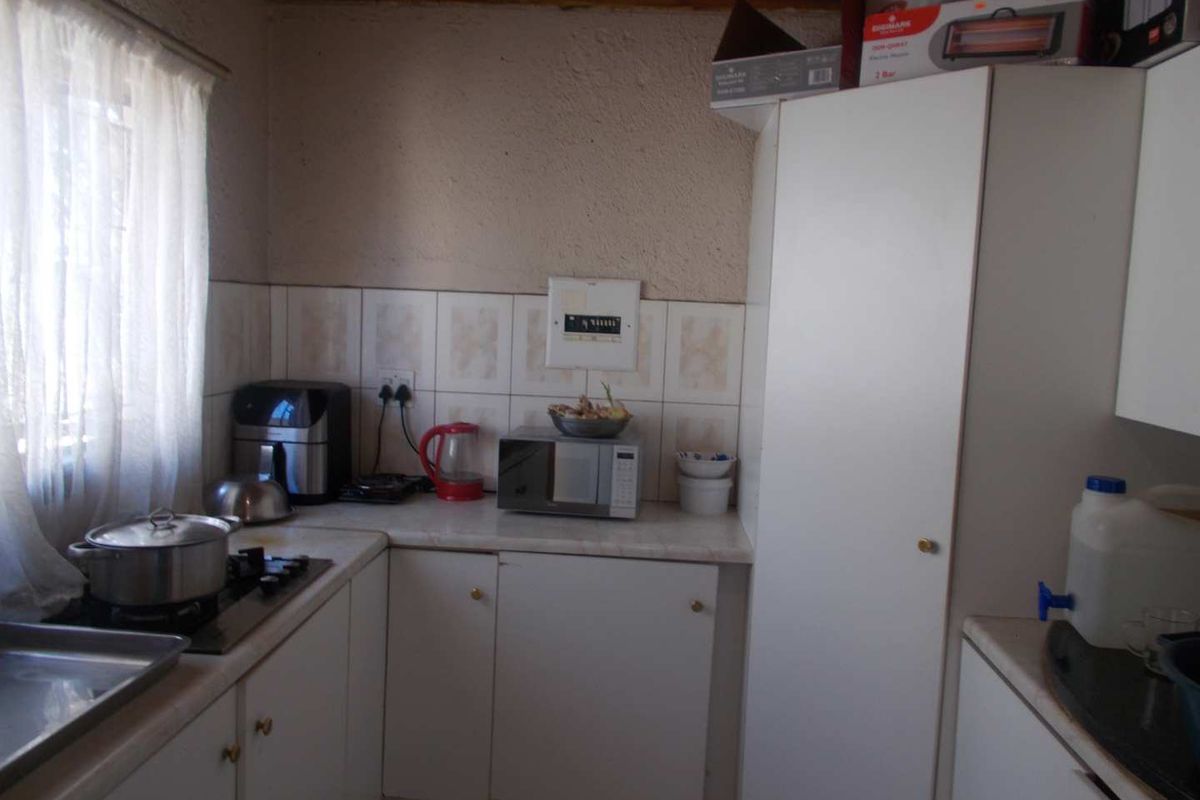 A compact kitchen featuring white built-in cabinetry, laminate countertops, a gas hob, and tiled backsplash, offering a functional layout with potential for modernization.