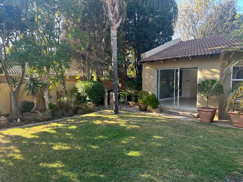 A well-maintained rear garden featuring a lawn, mature trees, and a sliding glass door providing access to the interior living space.