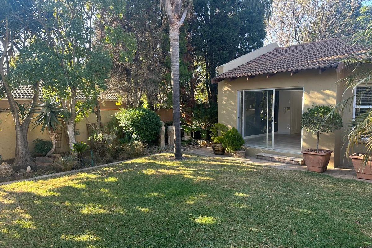 A well-maintained rear garden featuring a lawn, mature trees, and a sliding glass door providing access to the interior living space.