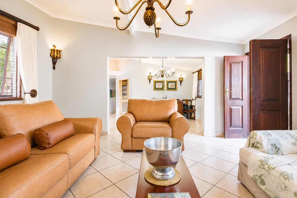 A well-maintained living room featuring tiled flooring, classic wall sconces, and a chandelier, with an open-plan flow into the adjacent dining area.