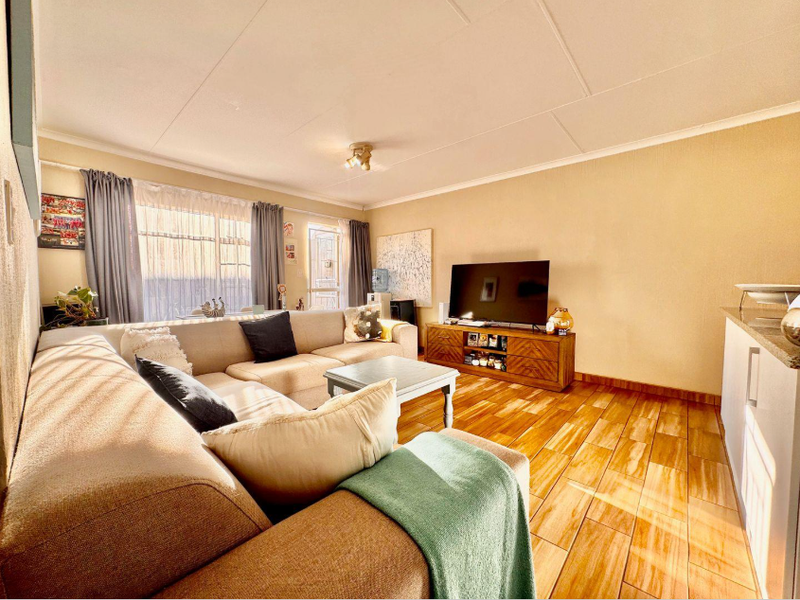 A bright and comfortable living room featuring wood-look tiled flooring, neutral walls, and a sliding glass door providing natural light.