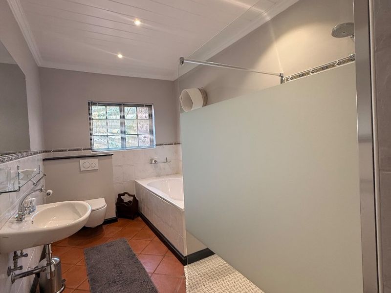 A well-maintained bathroom featuring a walk-in shower with a frosted glass screen, a built-in bathtub, a wall-mounted toilet, and a pedestal washbasin.