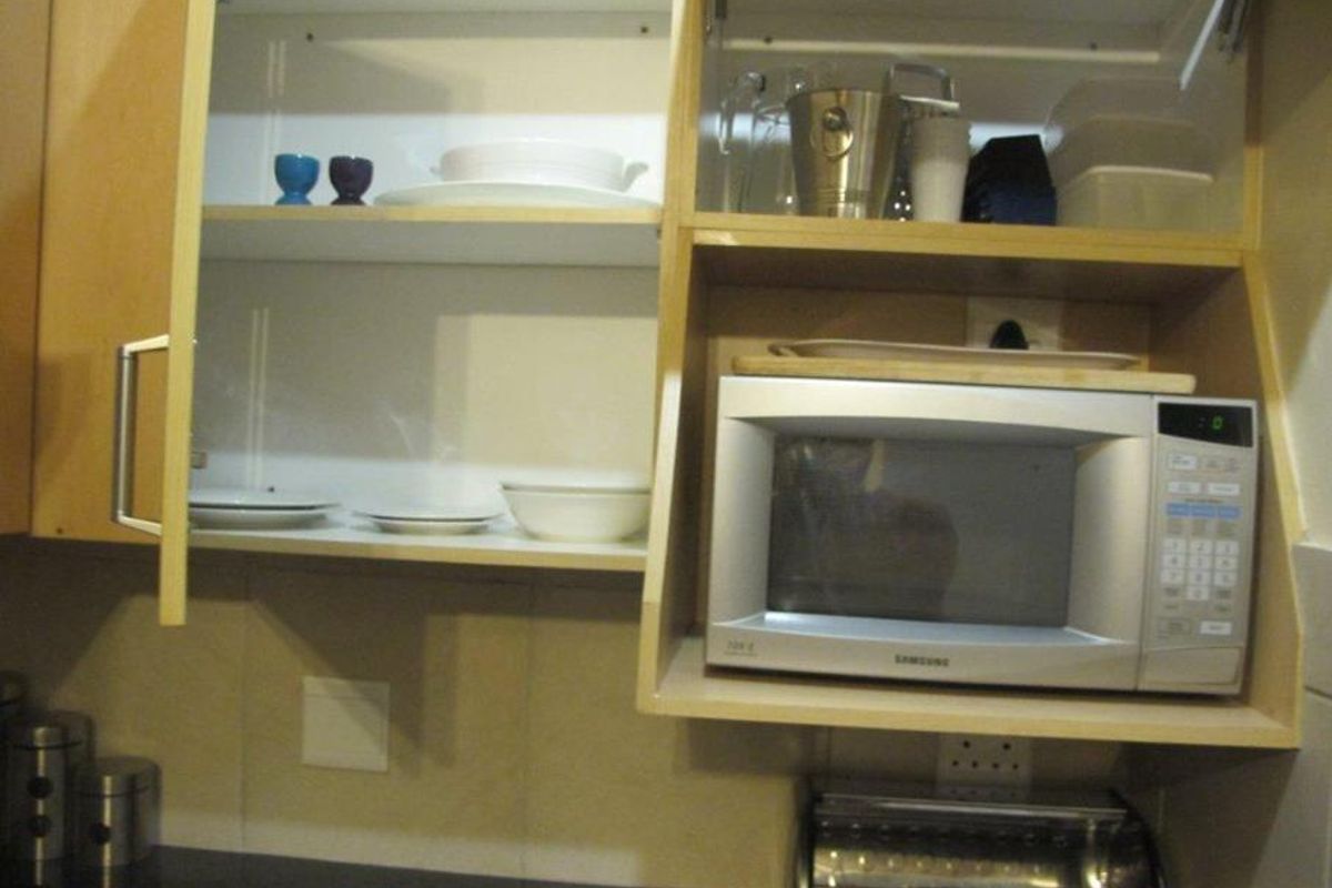 A close-up view of kitchen cabinetry featuring a built-in microwave, tiled backsplash, and storage shelving.