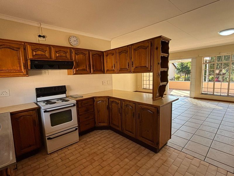 Open plan kitchen featuring timber cabinetry, tiled flooring, and a freestanding stove, flowing into a bright living area with access to an outdoor patio.