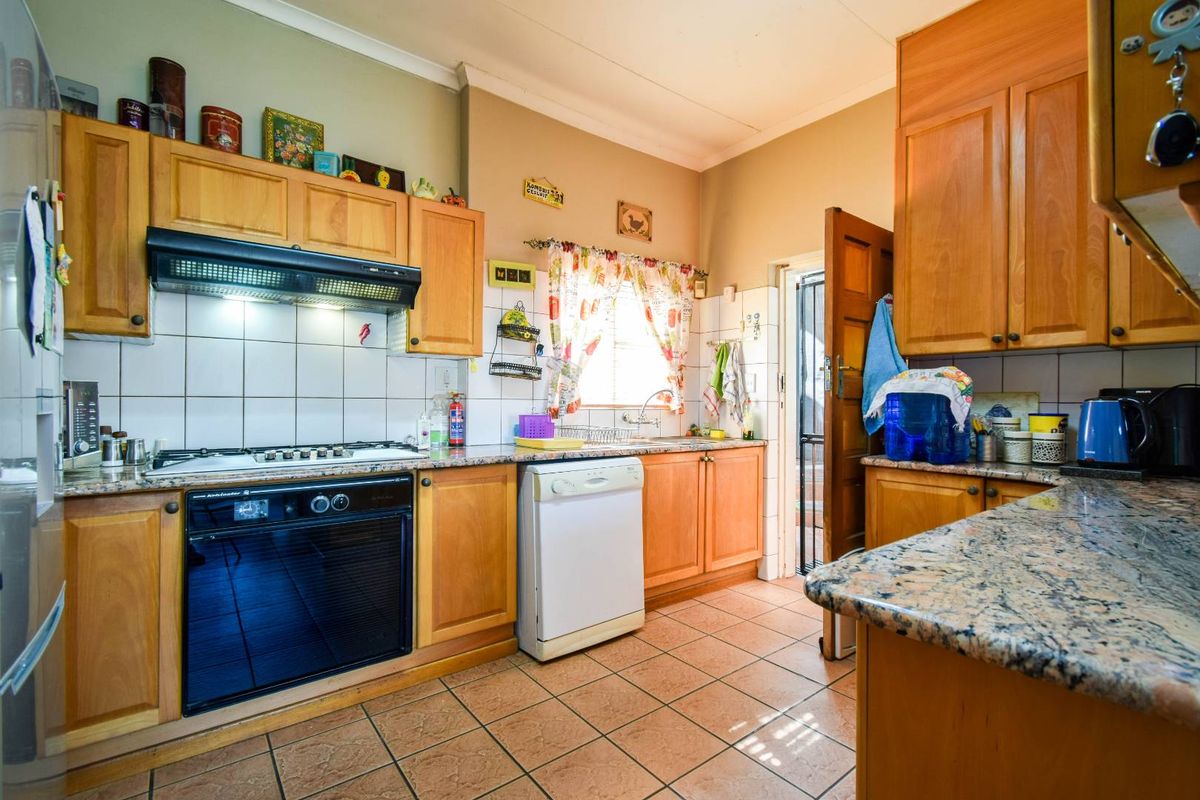 A functional kitchen featuring wooden cabinetry, granite countertops, tiled flooring, a built-in oven, gas hob, and an extractor fan.