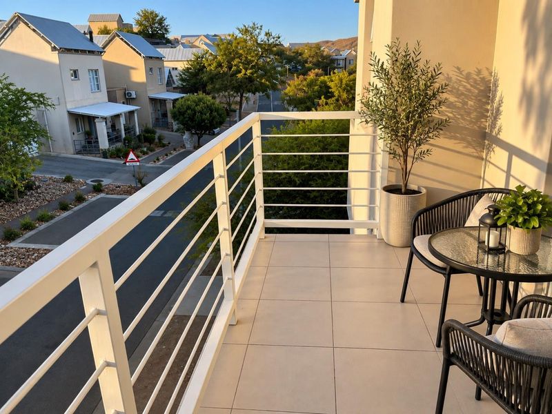 A well-maintained balcony featuring tiled flooring and a white metal balustrade, offering a pleasant view of the surrounding residential street.