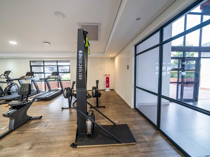 A well-maintained gym facility featuring laminate flooring, recessed lighting, ducted air conditioning, and large windows providing natural light.