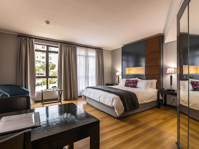 A well-maintained bedroom featuring laminate flooring, a modern built-in headboard with a recessed niche, and large windows allowing for natural light.