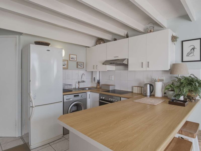 Compact kitchen featuring white cabinetry, wood-look countertops, tiled backsplash, and exposed ceiling beams, offering a functional and well-maintained cooking space.