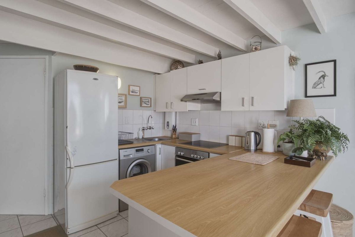 Compact kitchen featuring white cabinetry, wood-look countertops, tiled backsplash, and exposed ceiling beams, offering a functional and well-maintained cooking space.