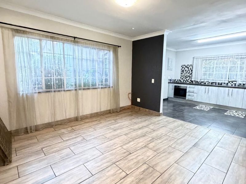 Spacious open-plan living and kitchen area featuring modern wood-look tile flooring, neutral walls, and a functional kitchen layout with built-in cabinetry and oven.