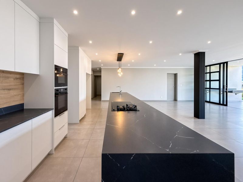 Modern open-plan kitchen and living area featuring a large island with stone countertop, built-in appliances, recessed lighting, and seamless access to the outdoor space.