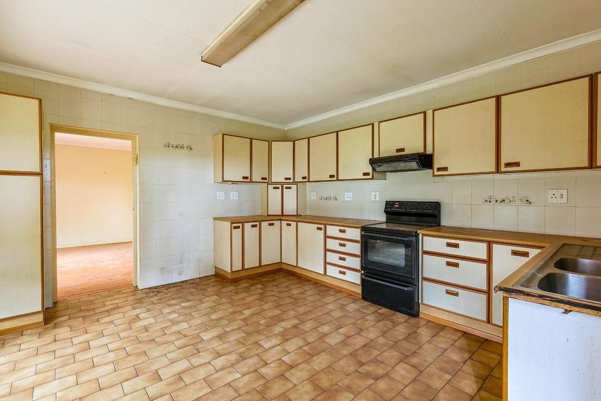 A dated kitchen featuring original cabinetry, a built-in oven with extractor fan, tiled flooring, and tiled splashbacks, offering potential for modernization.