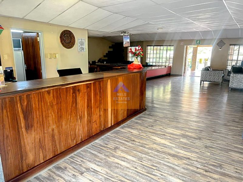 Spacious hotel reception area featuring a large built-in wooden counter, laminate flooring, and suspended ceiling tiles, offering a functional layout for guest services.