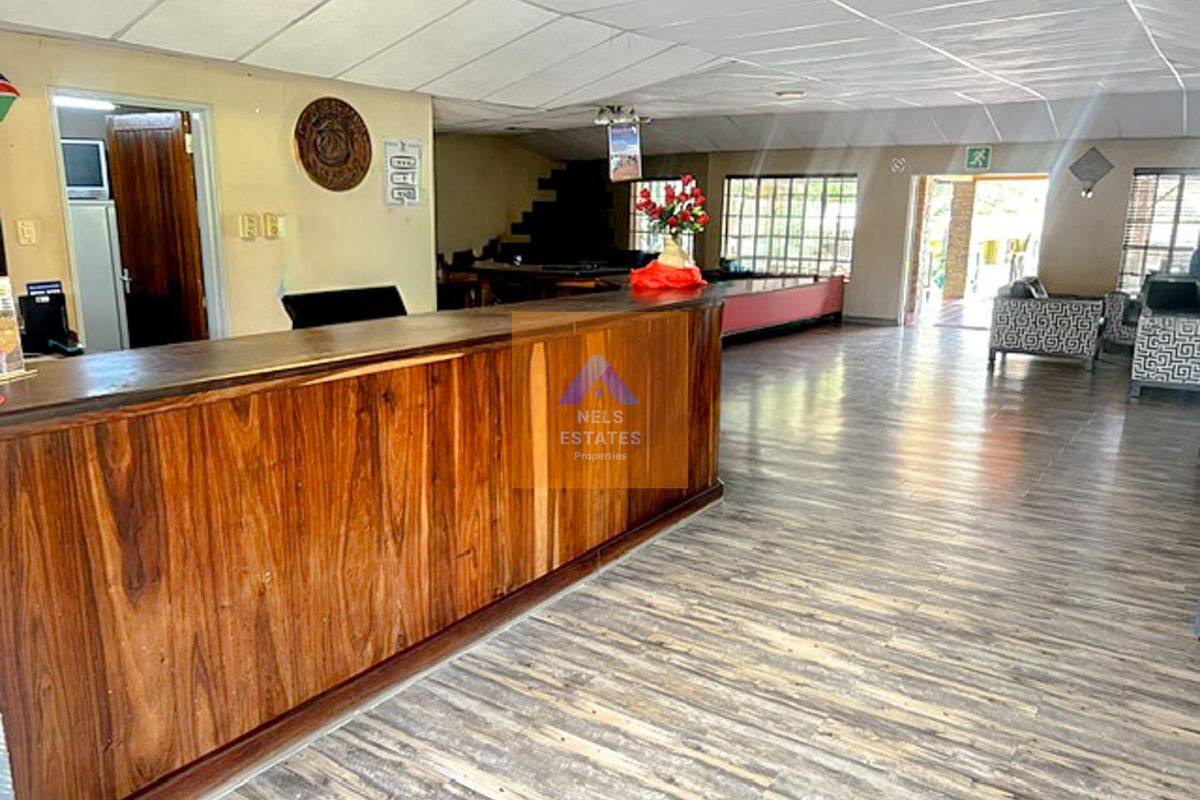 Spacious hotel reception area featuring a large built-in wooden counter, laminate flooring, and suspended ceiling tiles, offering a functional layout for guest services.