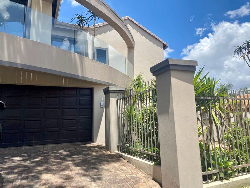 Front elevation of a modern residence featuring a paved driveway, secure garage access, and a prominent upper-level balcony with glass balustrading.