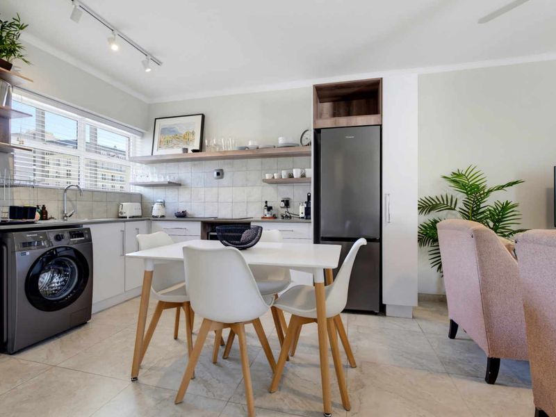 Modern open-plan kitchen and dining area featuring sleek white cabinetry, tiled flooring, track lighting, and integrated appliance housing.