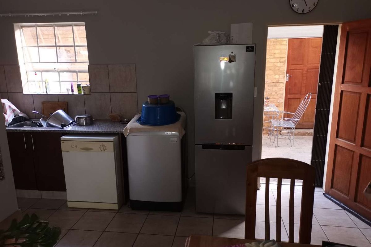 A functional kitchen area featuring tiled flooring, built-in cabinetry, and a stainless steel refrigerator, with direct access to an outdoor patio space.