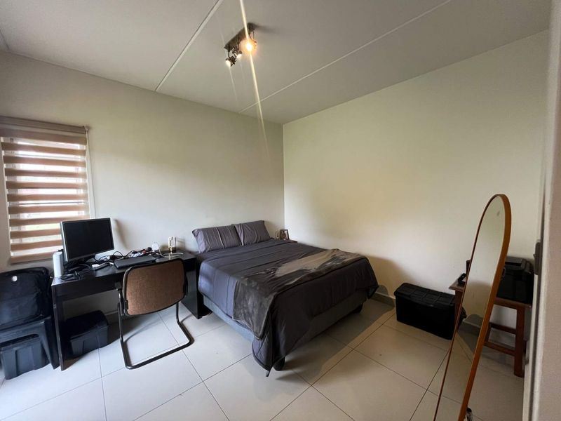 A functional bedroom featuring tiled flooring, neutral walls, and a window fitted with roller blinds, providing a simple and practical living space.