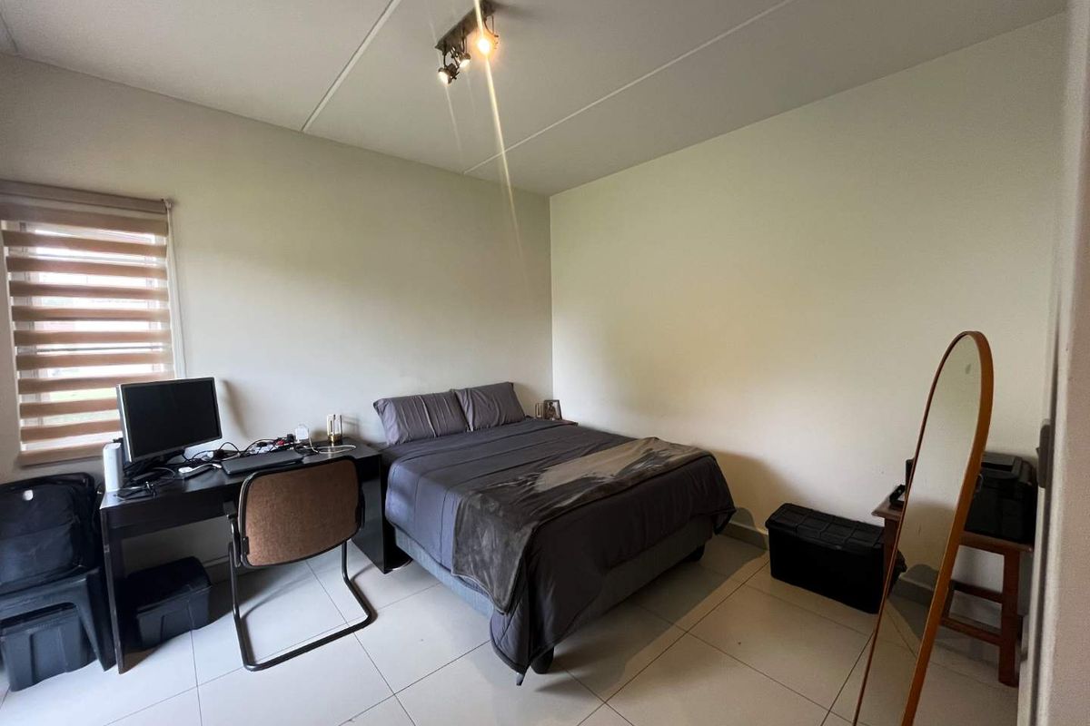 A functional bedroom featuring tiled flooring, neutral walls, and a window fitted with roller blinds, providing a simple and practical living space.