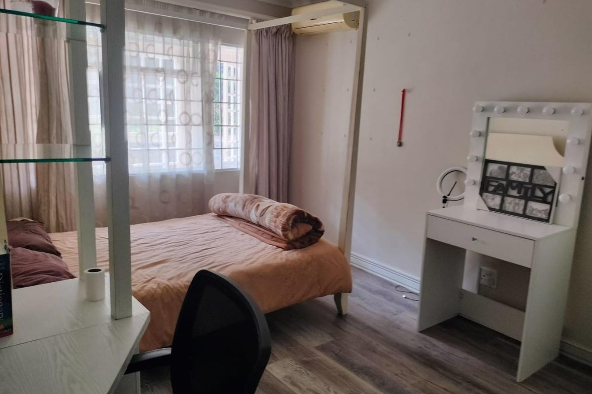 A bedroom featuring laminate flooring and a wall-mounted air conditioning unit, offering a functional space with neutral finishes.