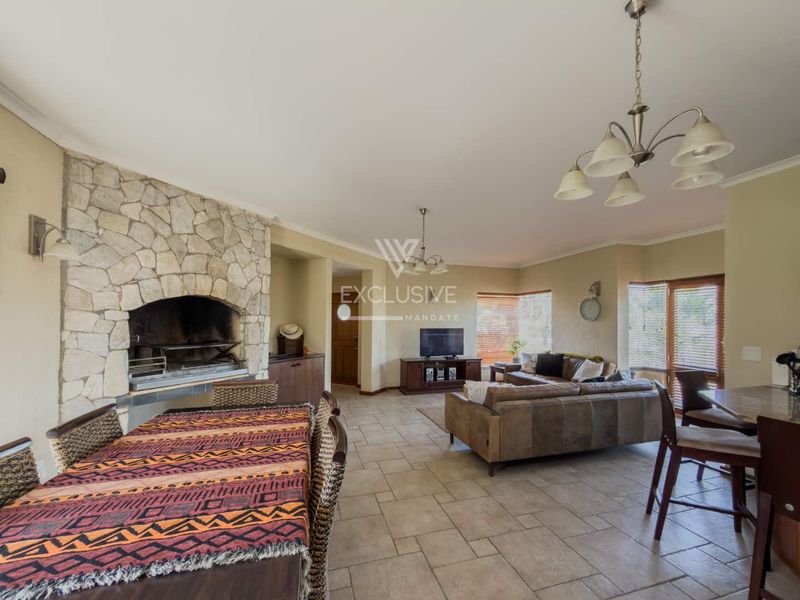Spacious open-plan living and dining area featuring a prominent stone-clad built-in fireplace, ceramic tile flooring, and classic chandelier lighting.