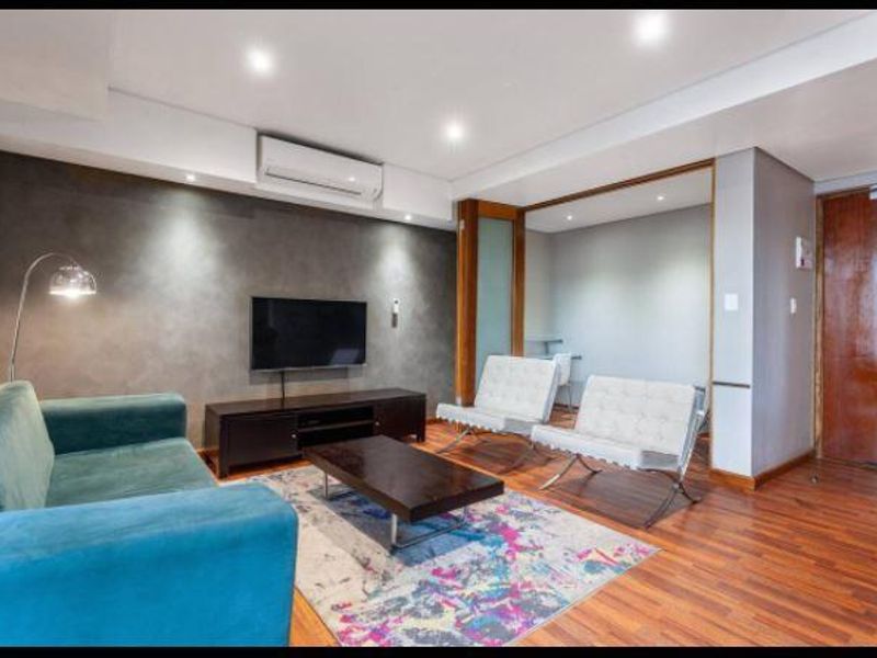 Modern living room featuring timber flooring, a feature wall, recessed downlighting, and a wall-mounted split-system air conditioner.