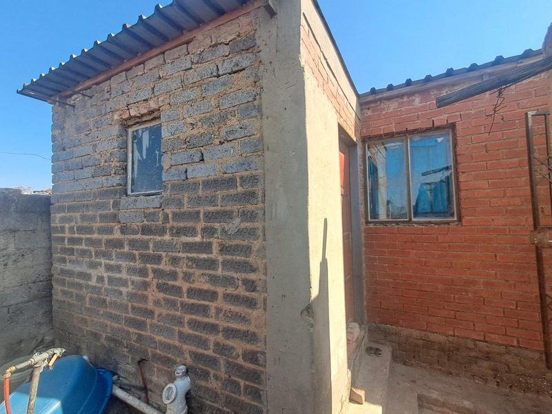 Rear exterior view of the property showing exposed brick construction, corrugated roofing, and basic metal window frames.