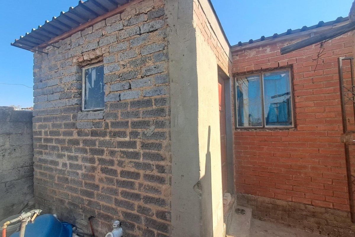 Rear exterior view of the property showing exposed brick construction, corrugated roofing, and basic metal window frames.