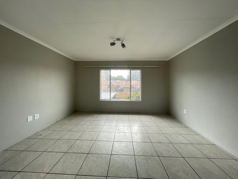A spacious, empty living area featuring neutral grey walls, tiled flooring, and a large window with security bars, offering a blank canvas for interior design.
