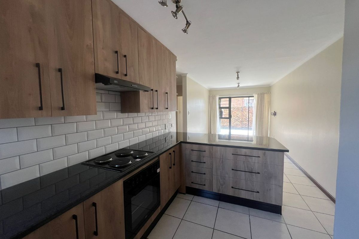 Modern kitchen featuring wood-finish cabinetry, black granite countertops, subway tile backsplash, and integrated appliances, flowing into an open-plan living area.