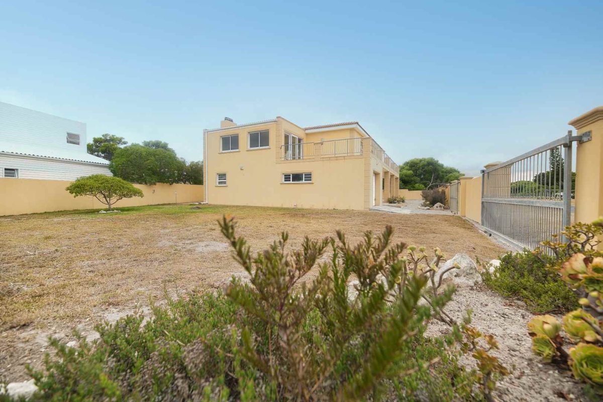 Rear view of the property featuring a spacious yard, perimeter wall, metal gate, and an upper-level balcony.