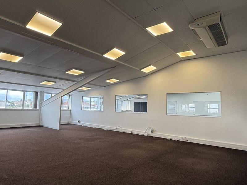 A spacious, open-plan office area featuring a suspended ceiling with recessed lighting, ducted air conditioning, large windows, and carpeted flooring.