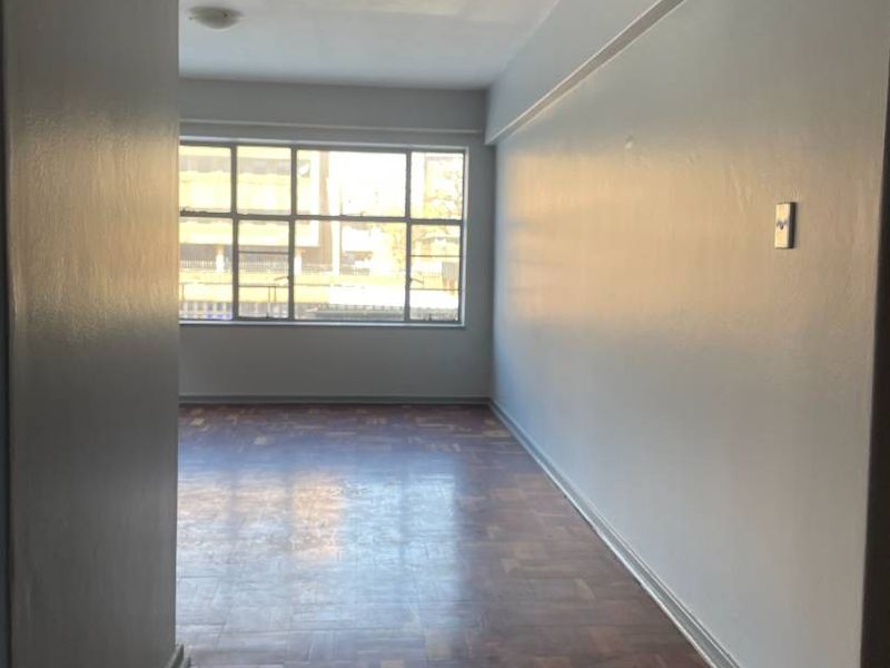 An empty living room featuring original parquet flooring and a large window providing natural light.
