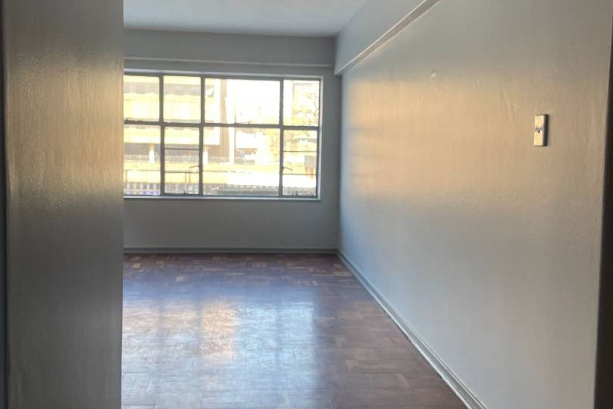 An empty living room featuring original parquet flooring and a large window providing natural light.