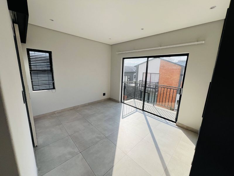 A bright, modern, and empty bedroom featuring large format floor tiles, recessed lighting, and a sliding door leading to a private balcony.