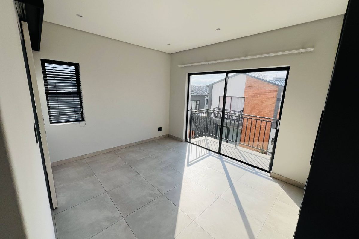 A bright, modern, and empty bedroom featuring large format floor tiles, recessed lighting, and a sliding door leading to a private balcony.