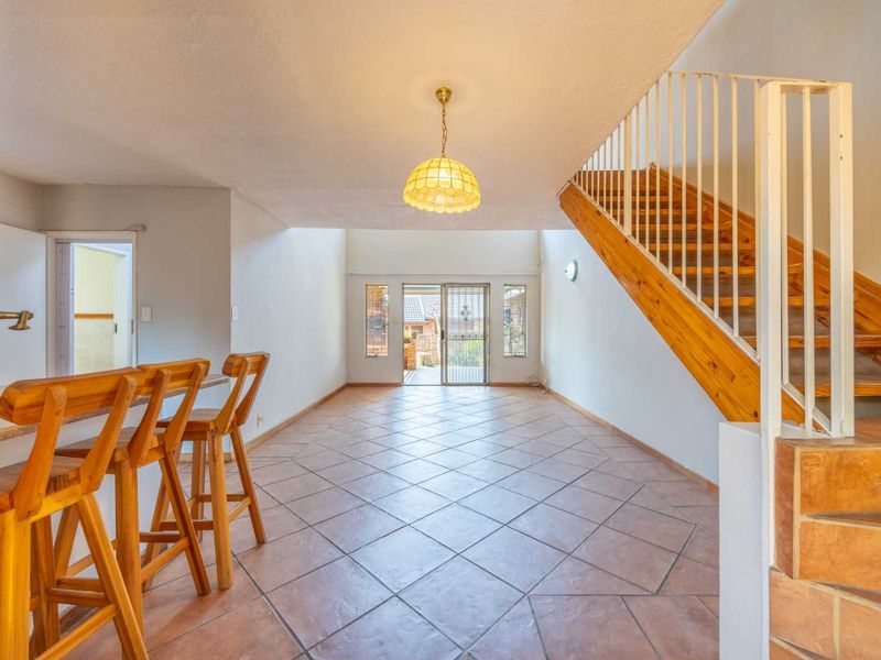 Open plan living area featuring tiled flooring, a wooden staircase with metal balustrade, and a breakfast counter leading to a rear patio.