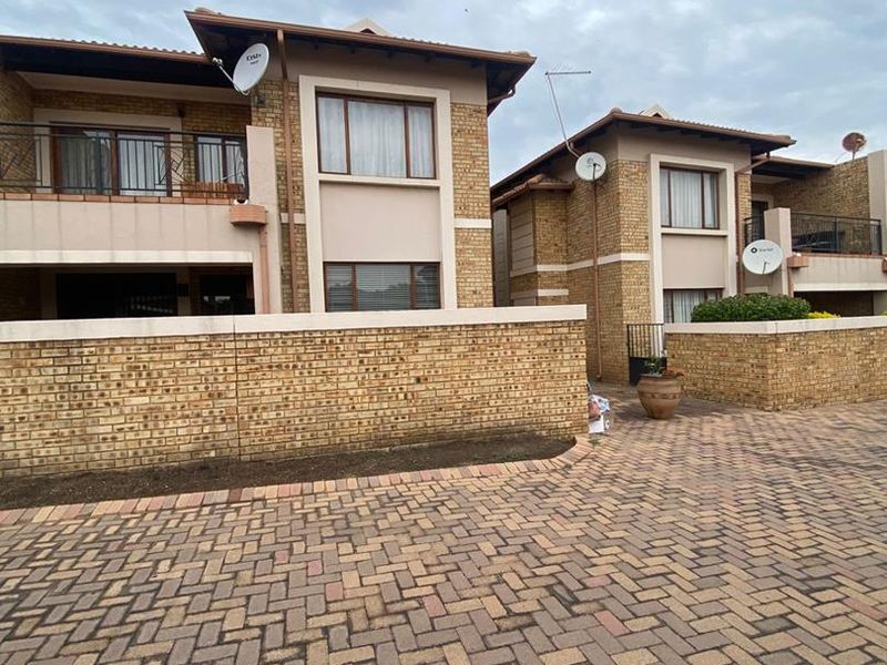 Exterior view of a face brick apartment complex featuring paved driveway access, boundary walls, and upper-level balconies.