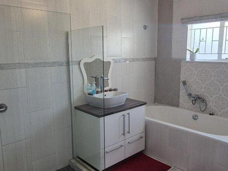 Modern bathroom featuring a walk-in shower, vessel sink vanity, and bathtub, with some unfinished tiling work visible near the ceiling.