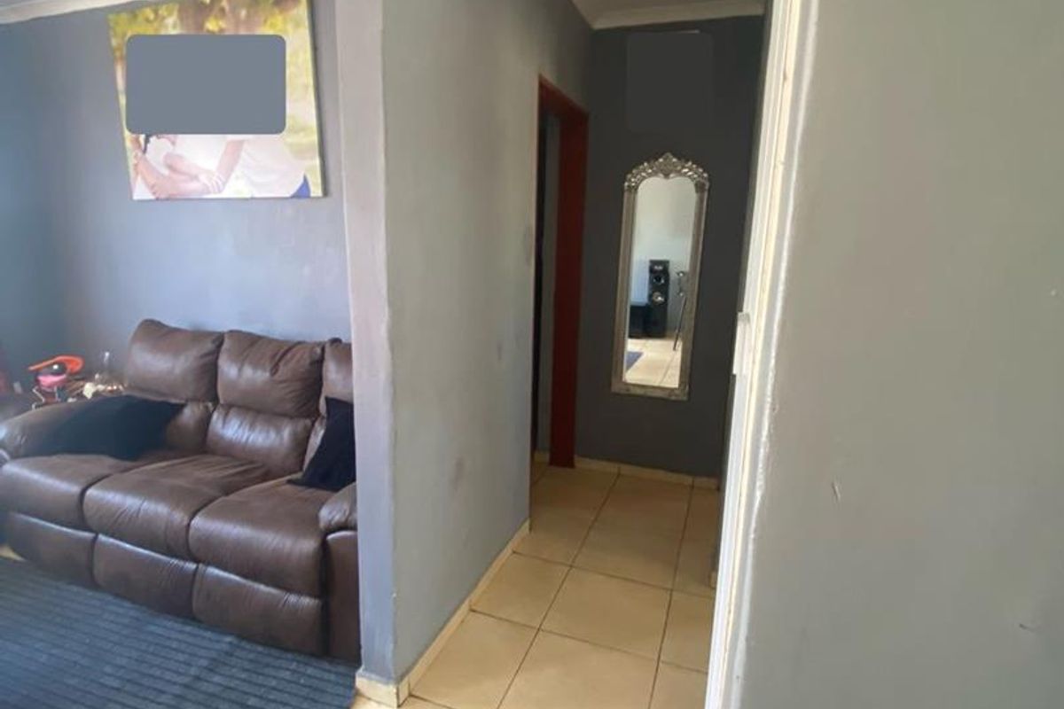A living room area featuring tiled flooring and grey painted walls, leading into a hallway space.