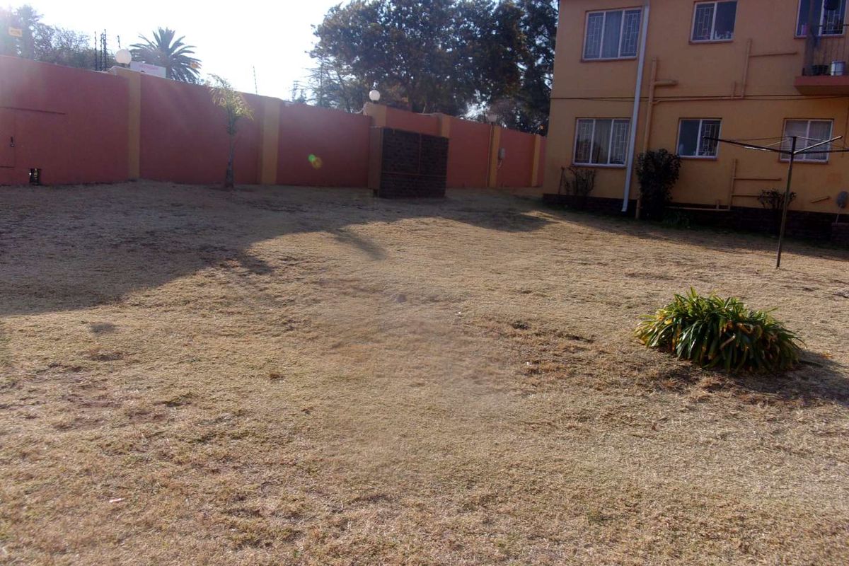 A view of the rear garden area featuring a large lawn, perimeter wall, and the rear facade of the apartment building.
