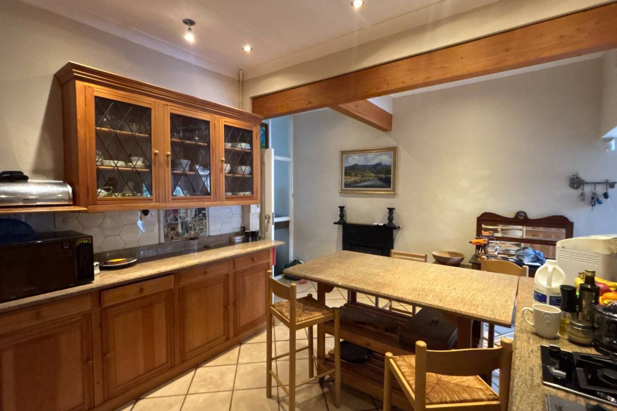 A spacious kitchen featuring warm wooden cabinetry, stone countertops, a tiled backsplash, and an exposed timber ceiling beam, creating a rustic and functional cooking space.